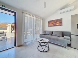 A modern living room with a grey sofa, a round coffee table, and a large window with sheer curtains. - Vacation home Danica by Interhome (Nin)