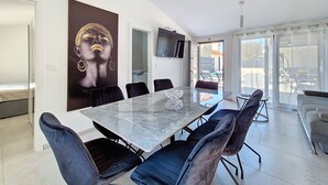 Een moderne eetruimte met een marmeren tafel, zwart beklede stoelen, een groot abstract schilderij en een televisie aan de muur.