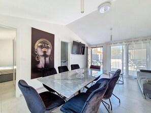 A modern dining area with a marble table, black upholstered chairs, a large abstract painting, and a TV mounted on the wall. - Vacation home Danica by Interhome (Nin)