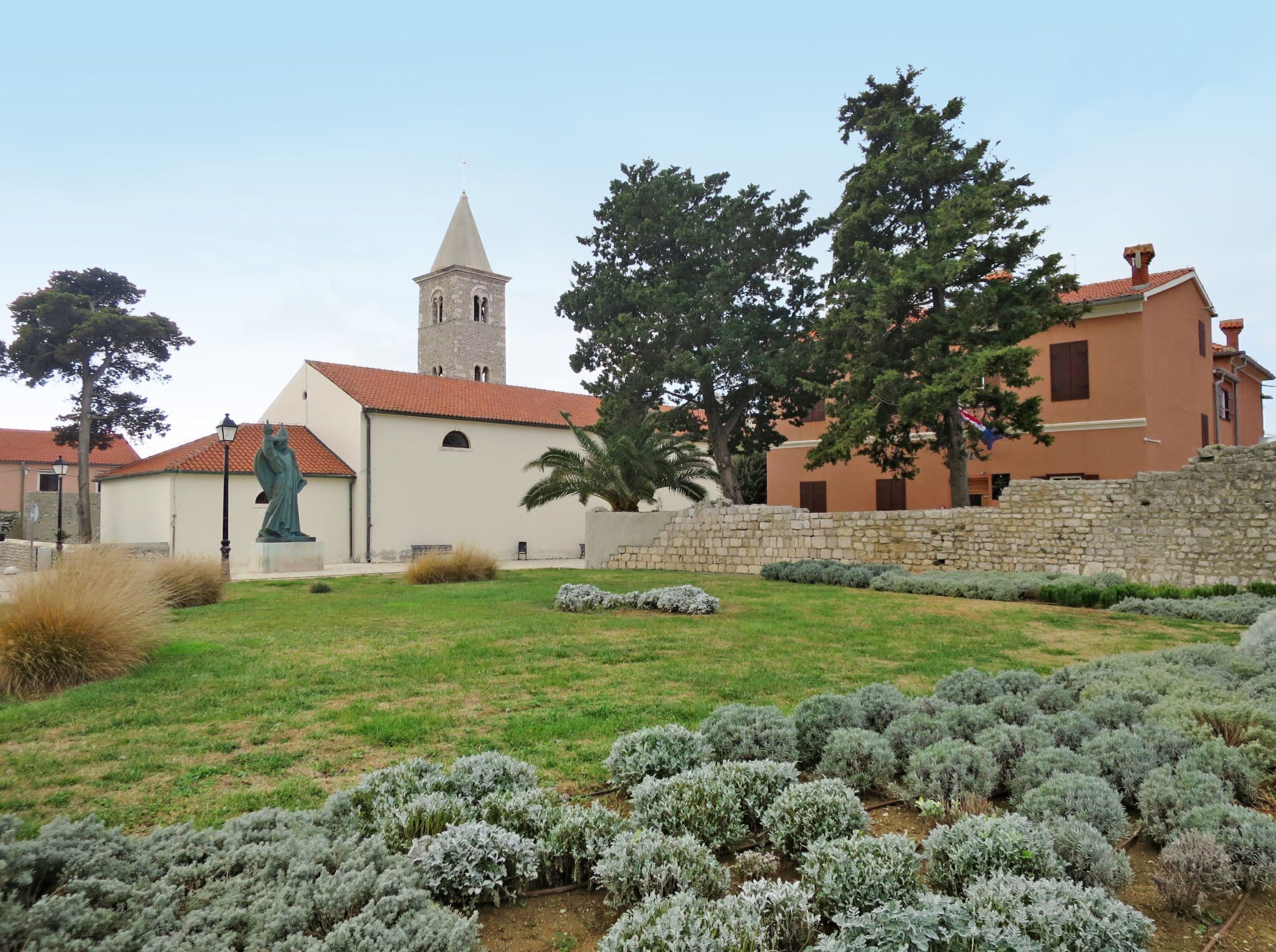 A church with a bell tower, a statue, and a garden with lavender bushes.