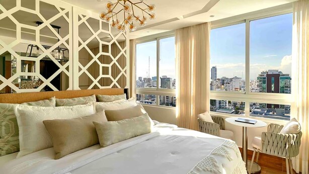 Ein Hotelzimmer mit einem großen Bett, Blick auf die Stadt, einem kleinen Tisch und einem Sessel.