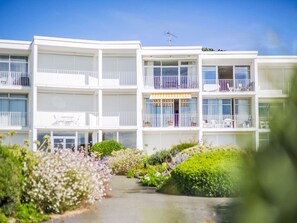 A multi-story hotel with balconies, a covered outdoor seating area, and a garden pathway. - Les Trois Iles by Interhome (Quiberon)