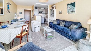 Een woonkamer met een bank, een eettafel, stoelen en een keuken op de achtergrond.