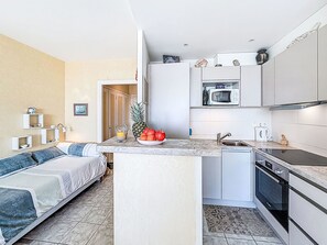 A compact living space with a kitchenette, a bed with a blue and white striped pillow, and a small dining area. - Les Trois Iles by Interhome (Quiberon)