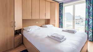 Ein Schlafzimmer mit einem Bett, einem Holzschrank und einem Fenster mit Blick auf Gebäude.