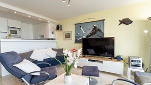 Ein modernes Wohnzimmer mit Sofa, Couchtisch, Fernseher und einer Küche im Hintergrund.
