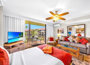 Ein Hotelzimmer mit Bett, Fernseher, Sofa, Couchtisch und einem Balkon mit Blick auf ein Resort.