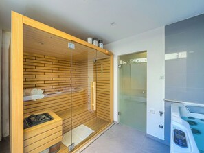 Eine Sauna mit Holzlamellen und Glastür, einem Handtuchhalter und einer kleinen Ablage mit Flaschen.