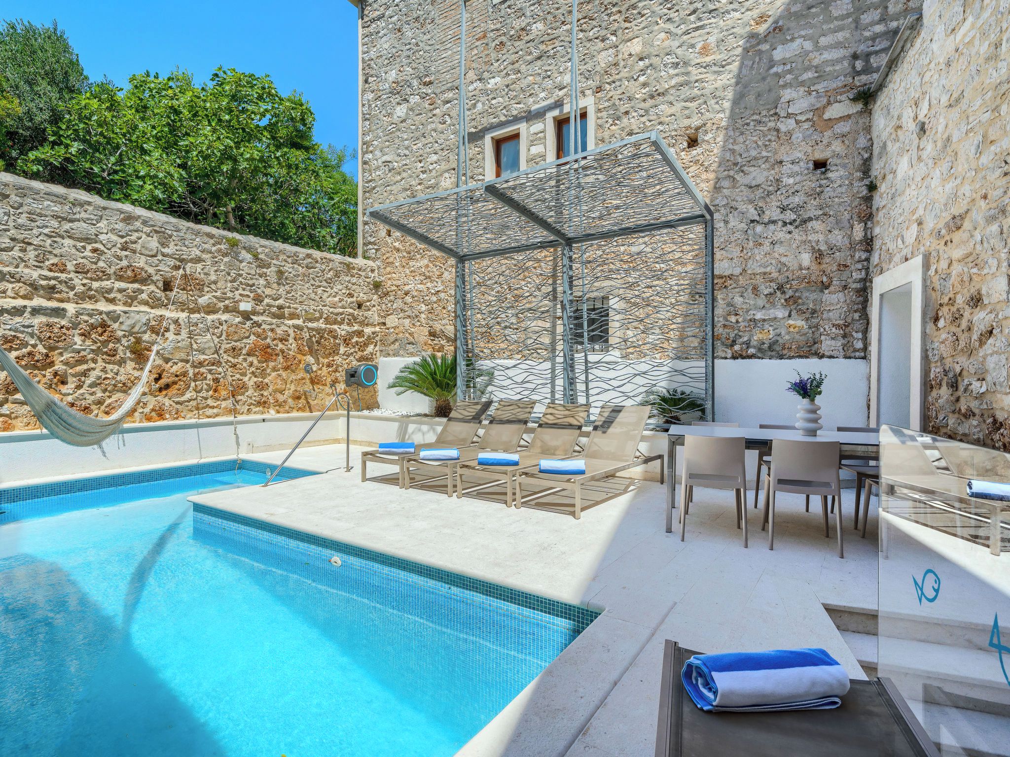 Un espace piscine agrémenté d’un mur en pierre, de chaises longues et d’une table avec des chaises.
