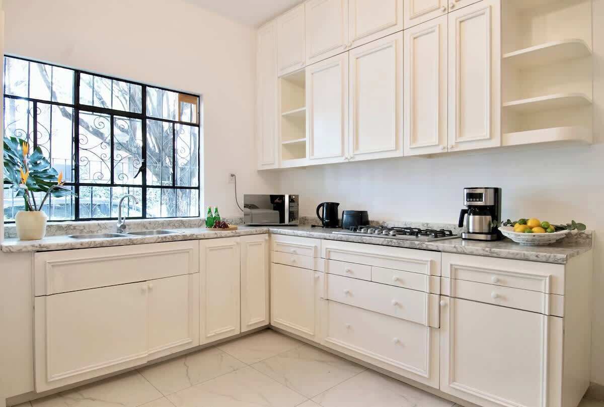 A modern kitchen with white cabinets, a marble countertop, a gas stove, a coffee maker, and a window with a view of trees.