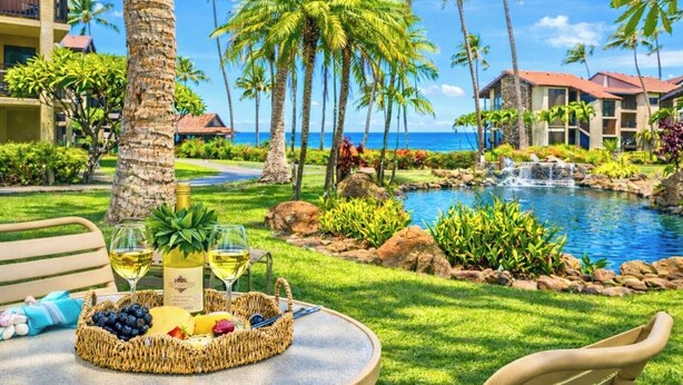 A tropical resort setting with a pool, palm trees, and a dining area with a table set for two. - Papakea Villas | Ocean View 2 BR Sleeps 8 | Car Incl. w/ 6+ Nights | PKD ML-3523 by KBM (Lahaina)