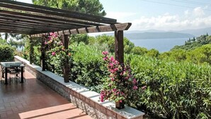 Un espace extérieur abrité, doté d’une table et de chaises, entouré d’une végétation luxuriante et offrant une vue sur une étendue d’eau.