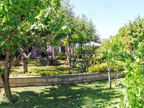A garden with a stone wall, various plants, and a building in the background. - Villa Cecilia by Interhome (Capoliveri)
