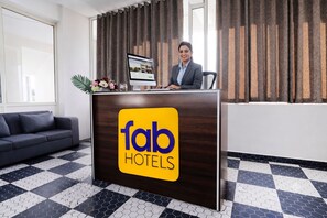 A hotel reception desk with a logo, a computer, and a person seated behind it. - Fabhotel Vishwas (Chhatrapati Sambhajinagar)