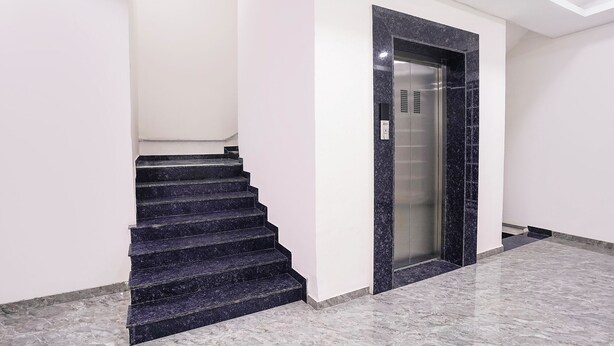 Un escalier menant à un ascenseur dans un immeuble moderne dont le sol est recouvert de marbre.