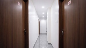 Un couloir bordé de portes en bois, portant les numéros de chambre 203 et 206, mène à un hall avec un sol en marbre et des murs blancs.