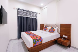 Una cama bien tendida con un colorido edredón de estampado geométrico, un cabecero de madera y una mesita de noche con un control remoto.