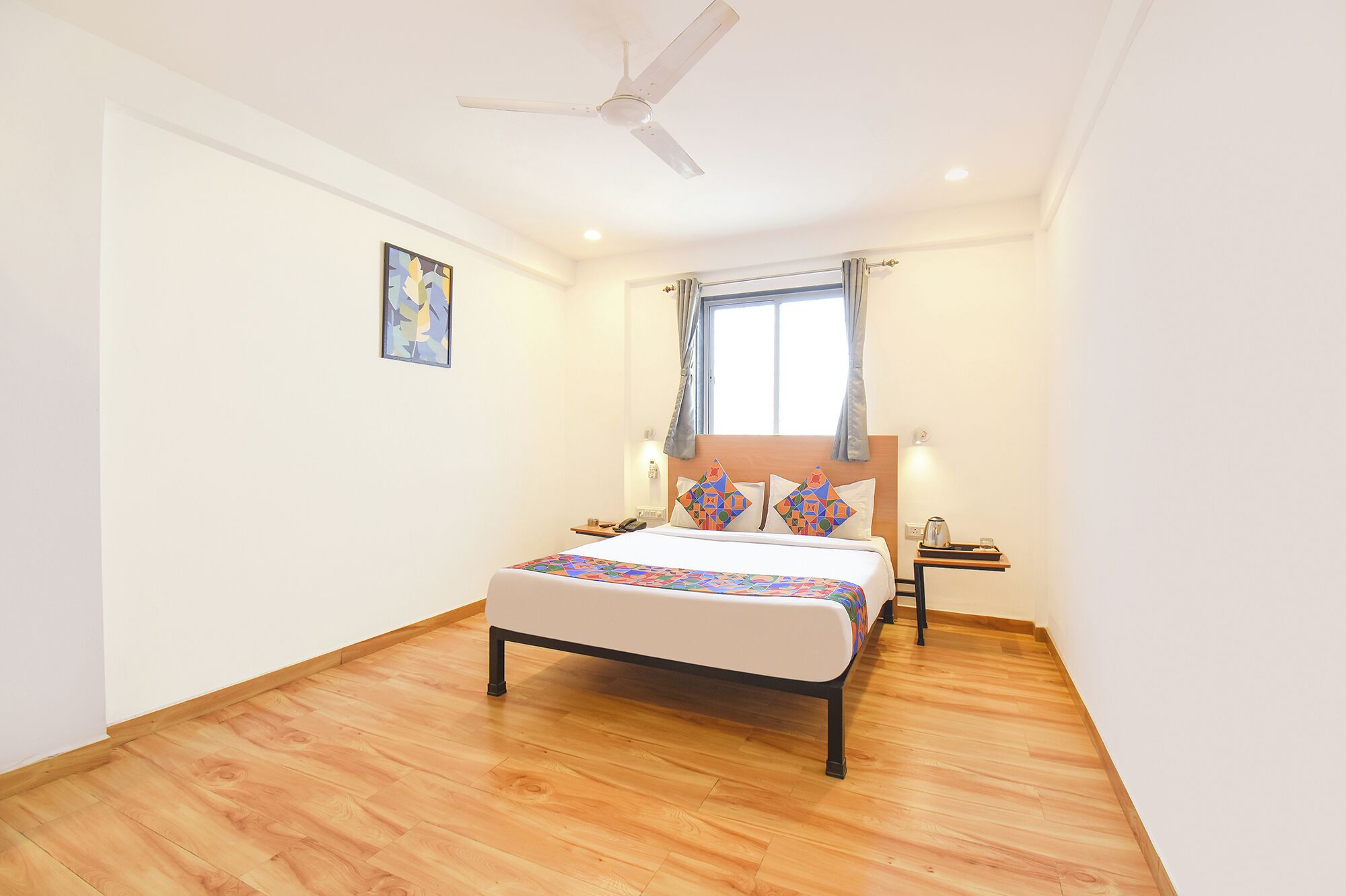 A bedroom with a bed, a ceiling fan, a window with curtains, and a bedside table with a lamp.