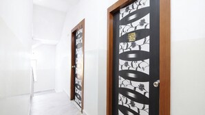 A hallway with two doors, one with a floral pattern and the other with a geometric design, leading to a room with white walls and a tiled floor. - Fabhotel Diamond Regency (Kolkata)