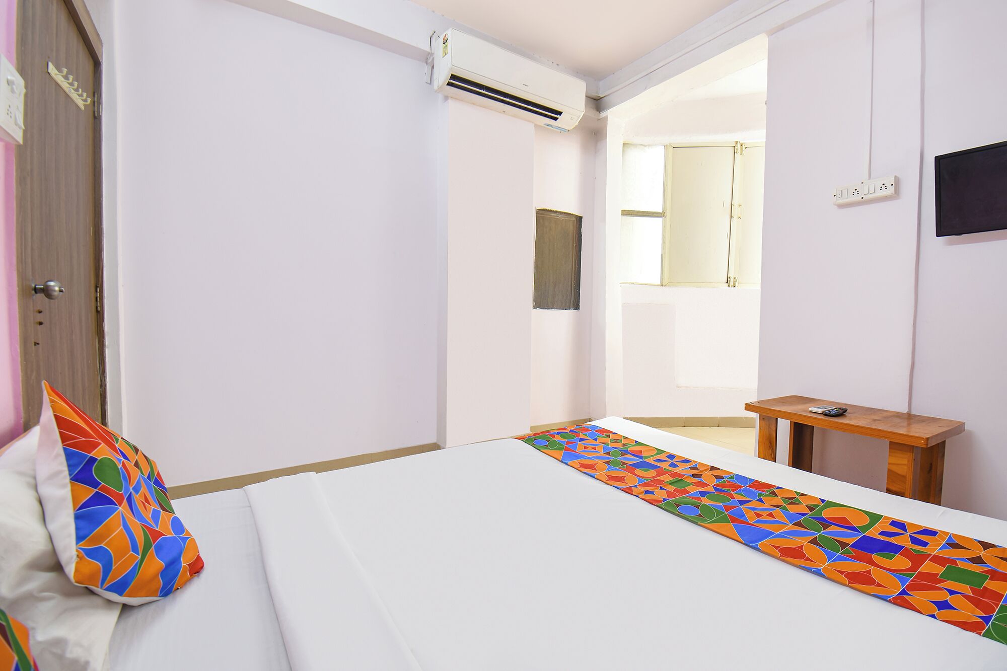 Una habitación de hotel con cama, una mesita, un televisor y un equipo de aire acondicionado.