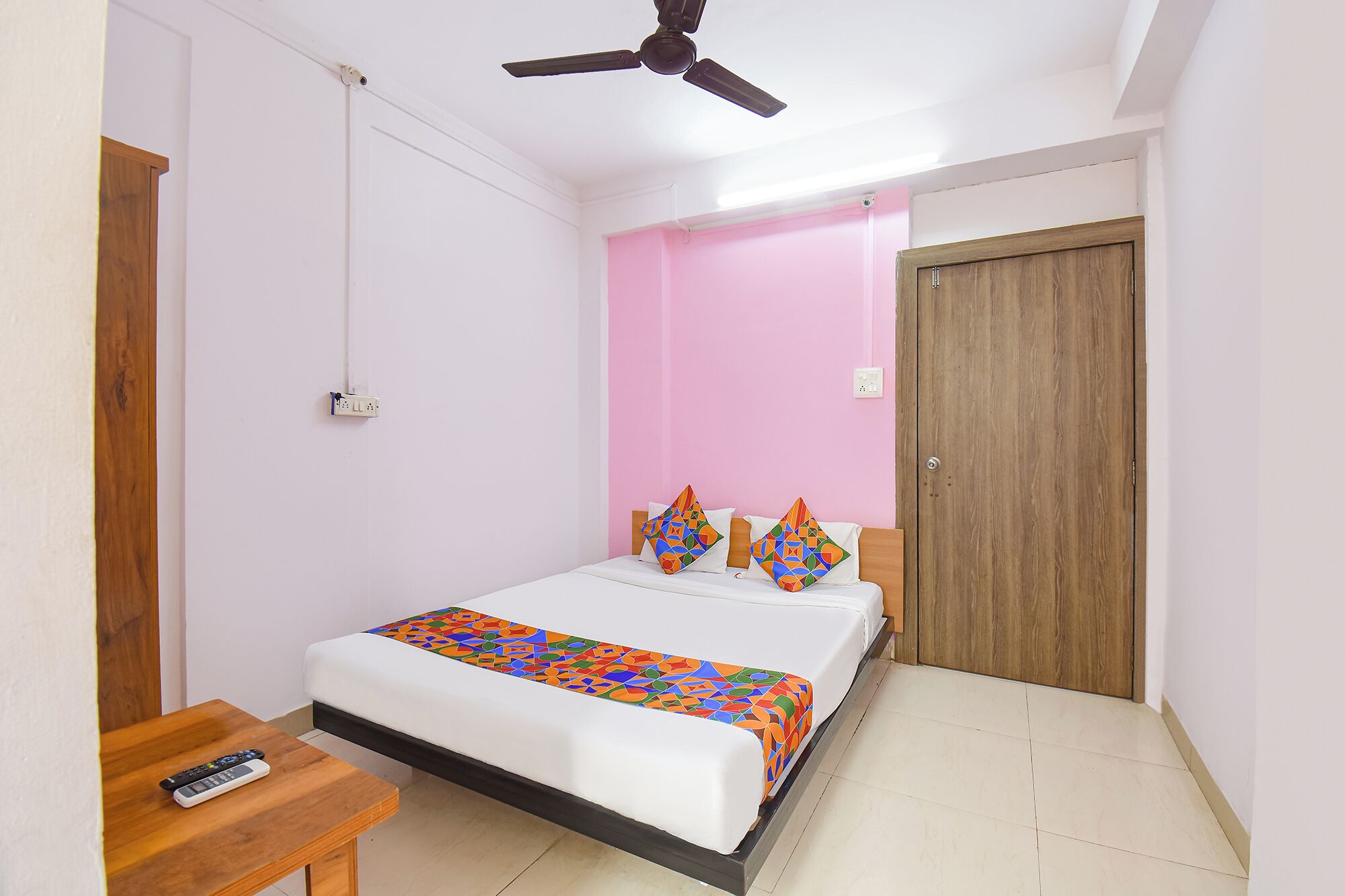 A bedroom with a bed, a ceiling fan, a wooden door, and a bedside table.