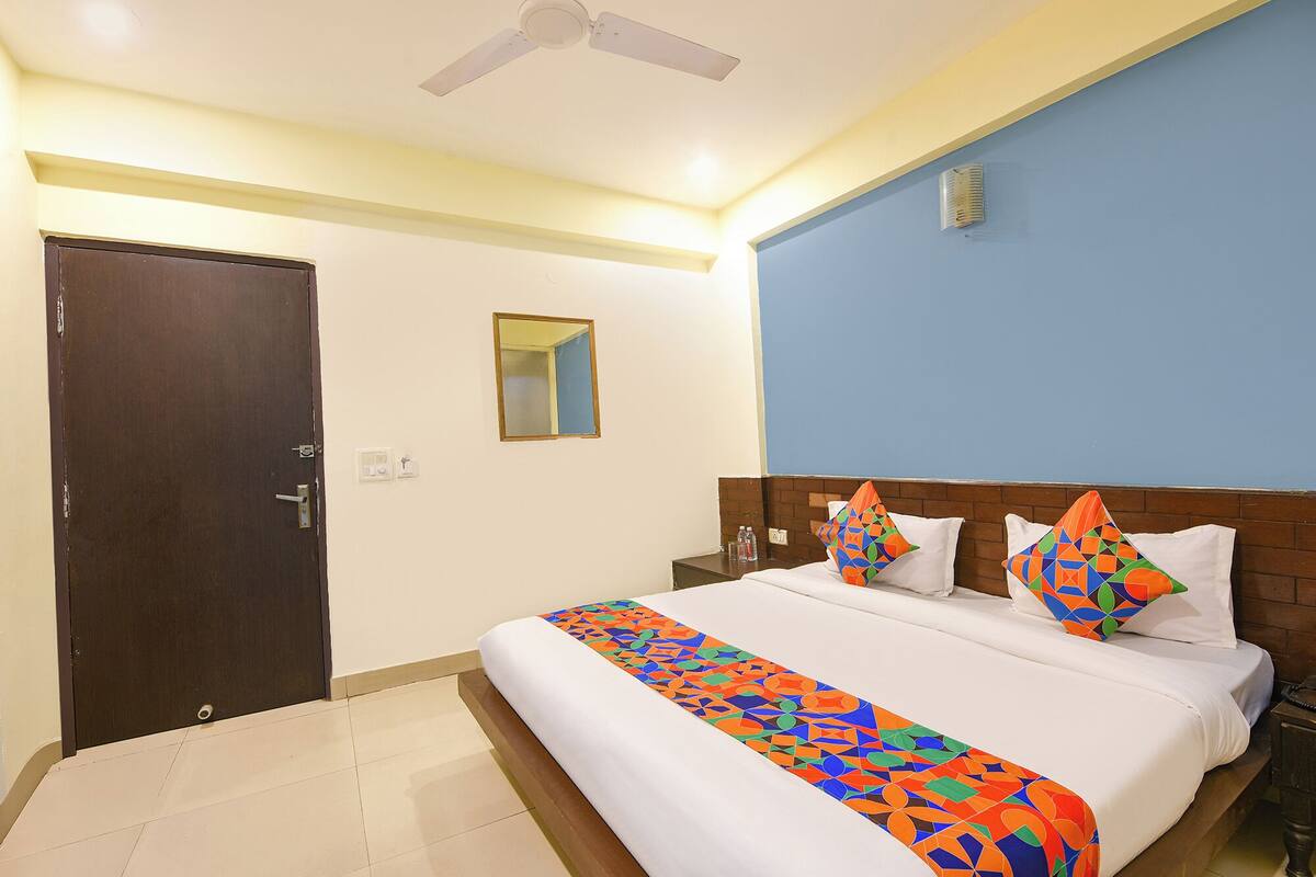 Una habitación de hotel con una cama, una mesita de noche, un espejo, una puerta y un ventilador de techo.