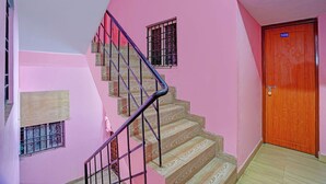 A staircase with a wooden finish, a pink wall, and a wooden door with a number plate. - Fabhotel Jay Jaga Residency (Chennai)