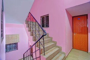 Una escalera con detalles de madera, una pared rosa y una puerta de madera con una placa numérica.