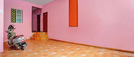 A pink-walled room with a scooter, a wooden floor, and a door with an orange panel.