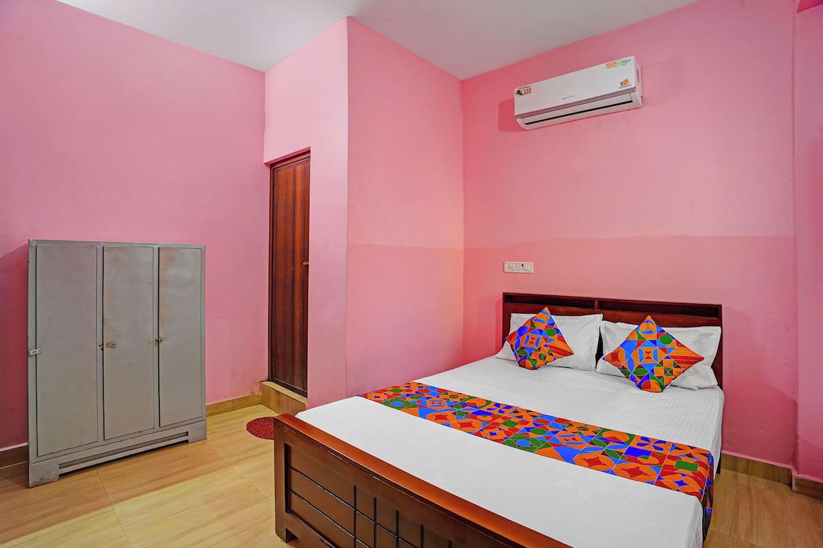 A bedroom with pink walls, a wooden bed, a gray wardrobe, and an air conditioning unit.