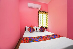 A room with pink walls, a bed with white bedding, colorful pillows, and a patterned bed runner.