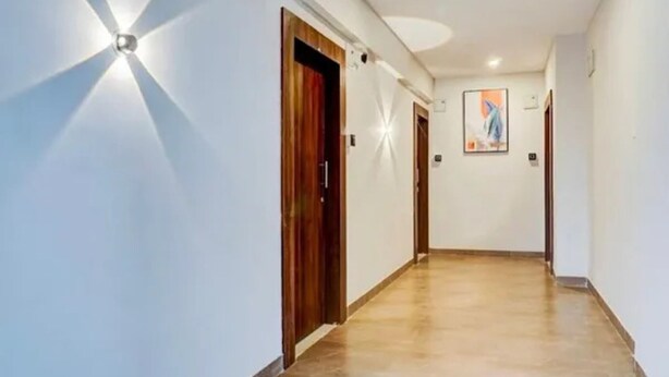 A hallway with a wooden door, a light fixture, and a painting on the wall. - Fabhotel Atithi Executive (Pune)