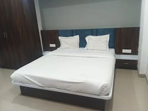 A neatly made bed with a white mattress and pillows, a dark headboard, and a wooden wardrobe to the left. - Fabhotel Atithi Executive (Pune)