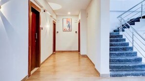 A hotel hallway with a marble floor, wooden doors, a painting on the wall, and a staircase with blue steps. - Fabhotel Atithi Executive (Pune)