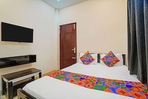 Habitación de hotel con cama, televisor montado en la pared, puerta de madera y ventana con cortinas.