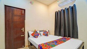 Un dormitorio con una puerta de madera, una cama con almohadones de colores, una colcha estampada y una cortina.