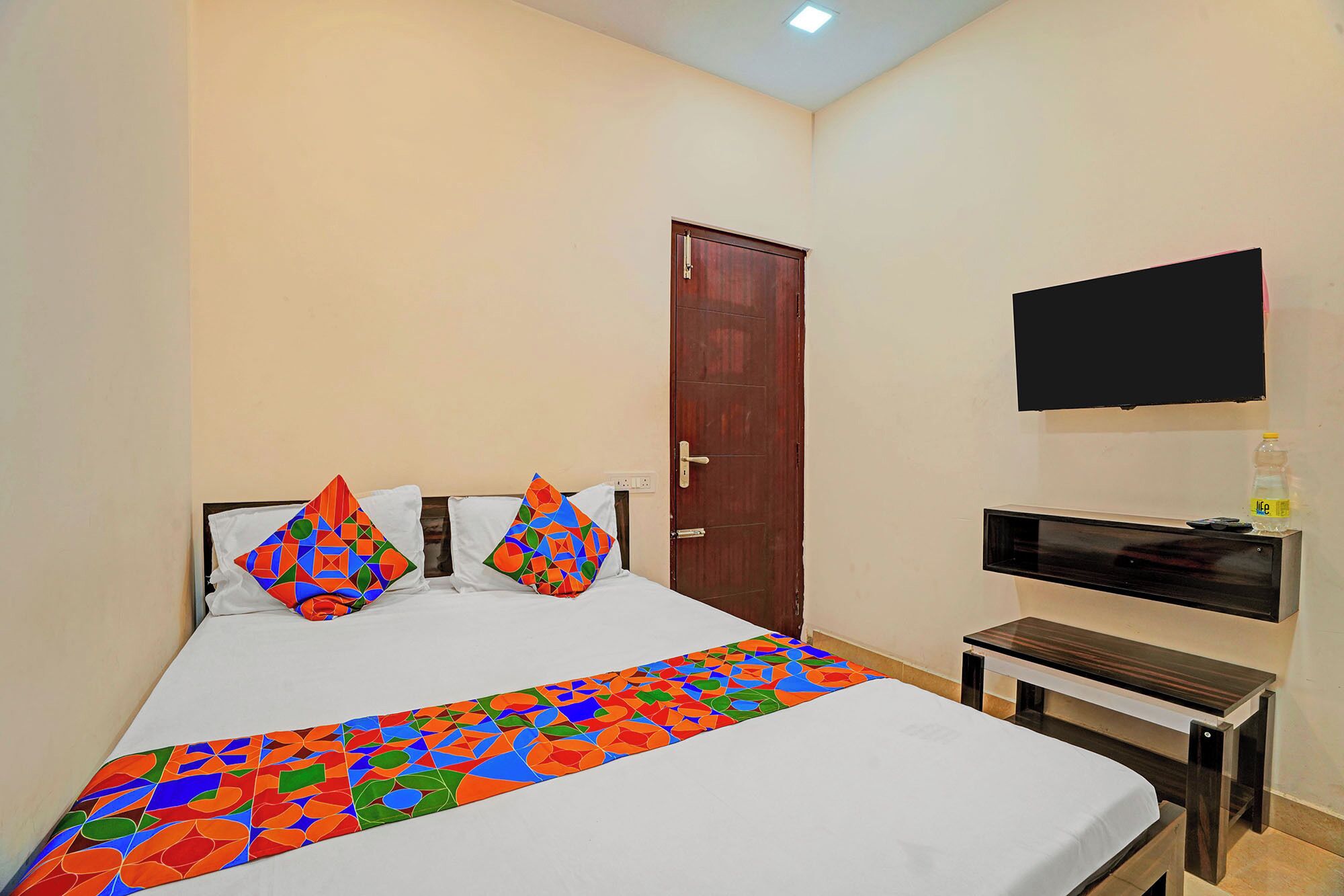 A hotel room with a bed, a TV mounted on the wall, a wooden door, and a small table.