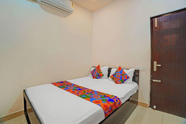 A single bed with a colorful bedspread and two geometric pillows, a wooden door, and a wall-mounted air conditioning unit. - Fabhotel Gold Residency (Chennai)