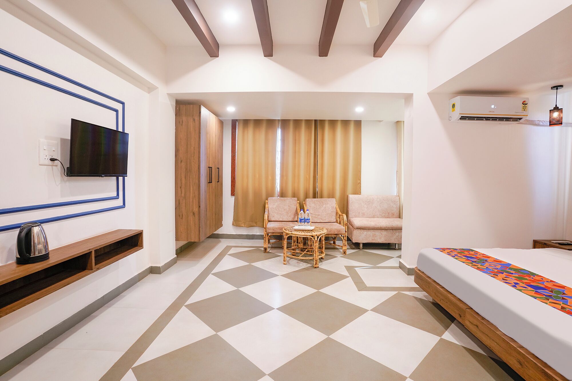 Habitación de hotel con televisor, cama, zona de estar con sillas y una mesa de centro, además de un suelo estampado.