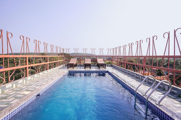 A rooftop pool with a clear view of the surrounding landscape, including hills and palm trees.
