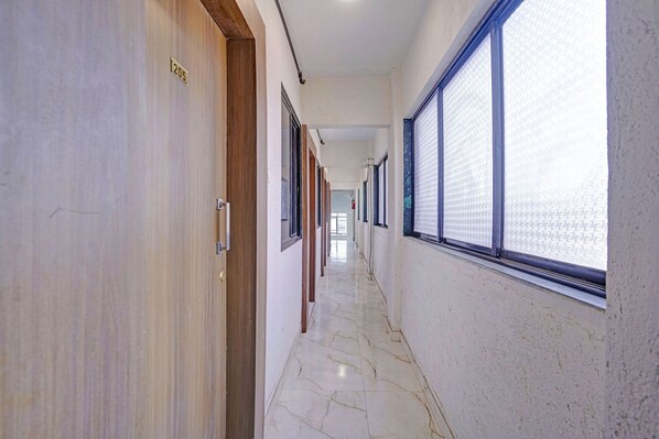 A hallway with wooden doors, a marble floor, and large windows with patterned blinds. - Fabhotel Red Rose Palghar (Vasai)