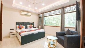 A modern hotel room with a bed, a sofa, a small round table, and large windows. - Fabhotel Park View (New Delhi)