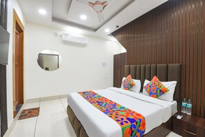 Une chambre d’hôtel avec un lit, une table de chevet avec une bouteille d’eau, un miroir et un ventilateur de plafond.