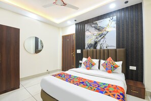 Une chambre d’hôtel moderne avec un grand lit, un miroir rond, un ventilateur de plafond et un mur décoré d’un motif imitant le marbre.