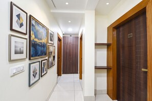 Un couloir avec des œuvres d’art encadrées accrochées aux murs, une porte en bois portant un numéro et un interrupteur.