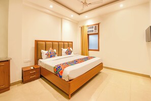 Une chambre à coucher comprenant un lit, une table de chevet, une fenêtre avec des rideaux, un ventilateur de plafond et un climatiseur fixé au mur.