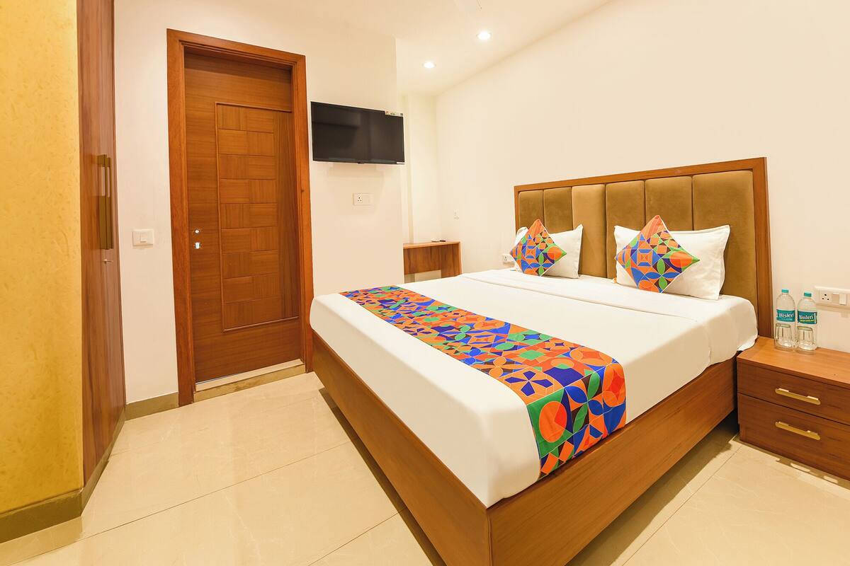 Hotelkamer met een houten bed, een aan de muur bevestigde televisie en een nachtkastje met flessen.