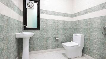 A bathroom with a pedestal sink, a toilet, and a mirror with a fan above it.