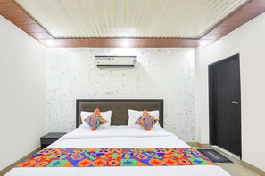 A bedroom with a bed, an air conditioning unit, a door, and a patterned carpet. - Fabhotel Mb Residency (New Delhi)