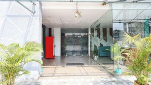 A modern building entrance with glass doors, a red cabinet, and potted plants. - Fabhotel Lorven Grand (Visakhapatnam)
